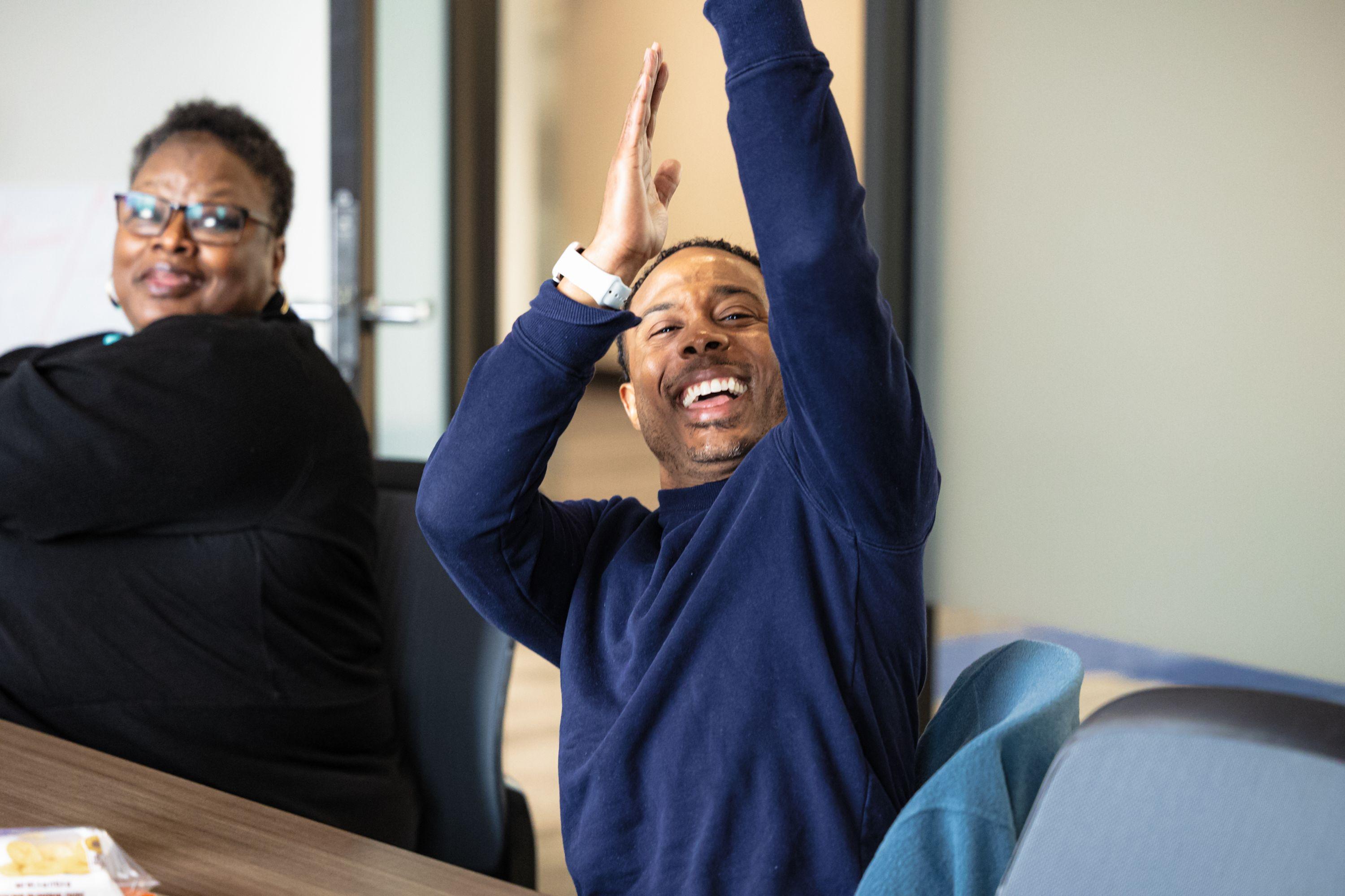 A happy Black man celebrating with his arms in the air during an Adaptive Equity Leadership Institute meeting 