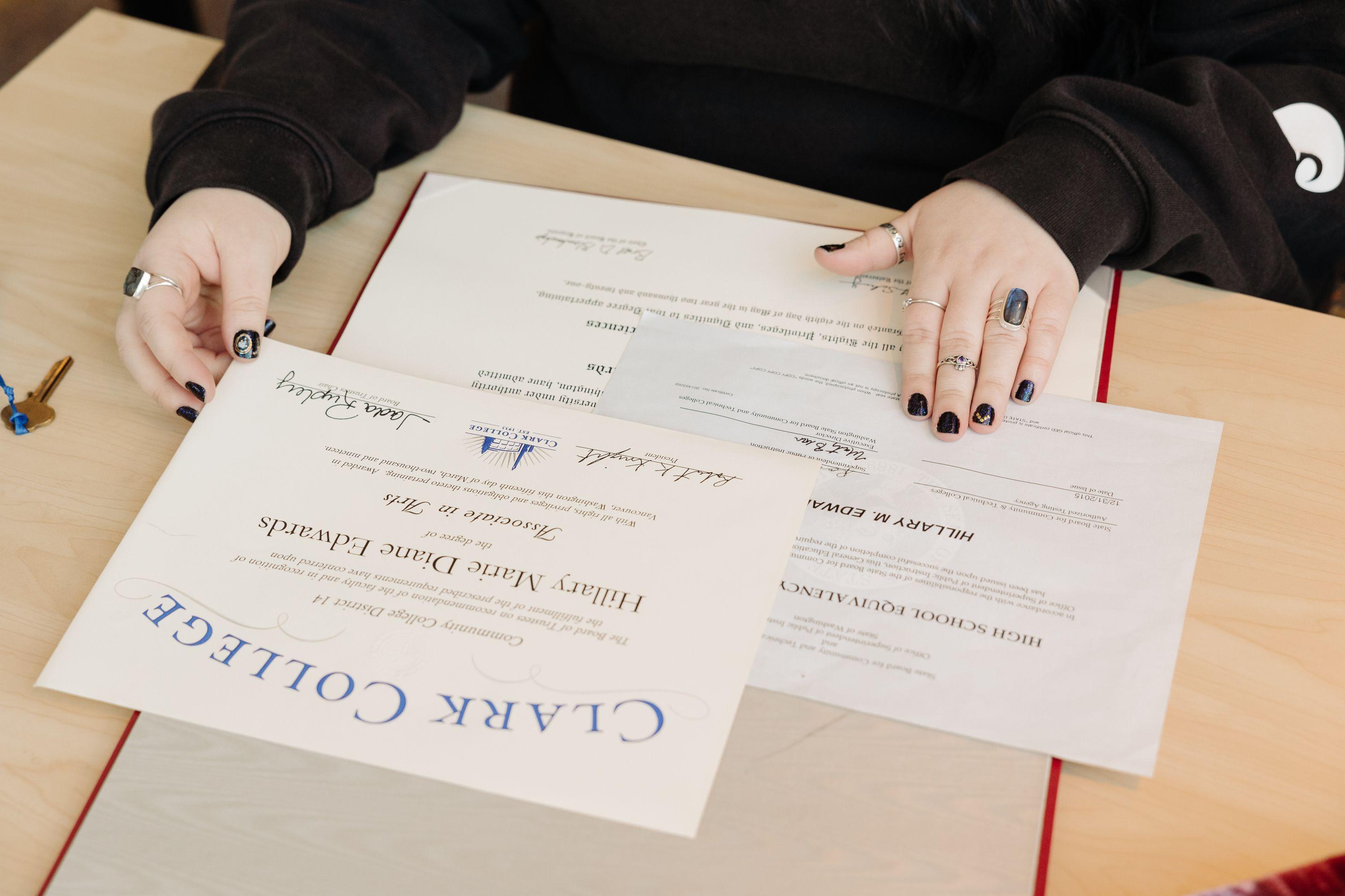 Clark College diploma on table with graduated student's hands in frame