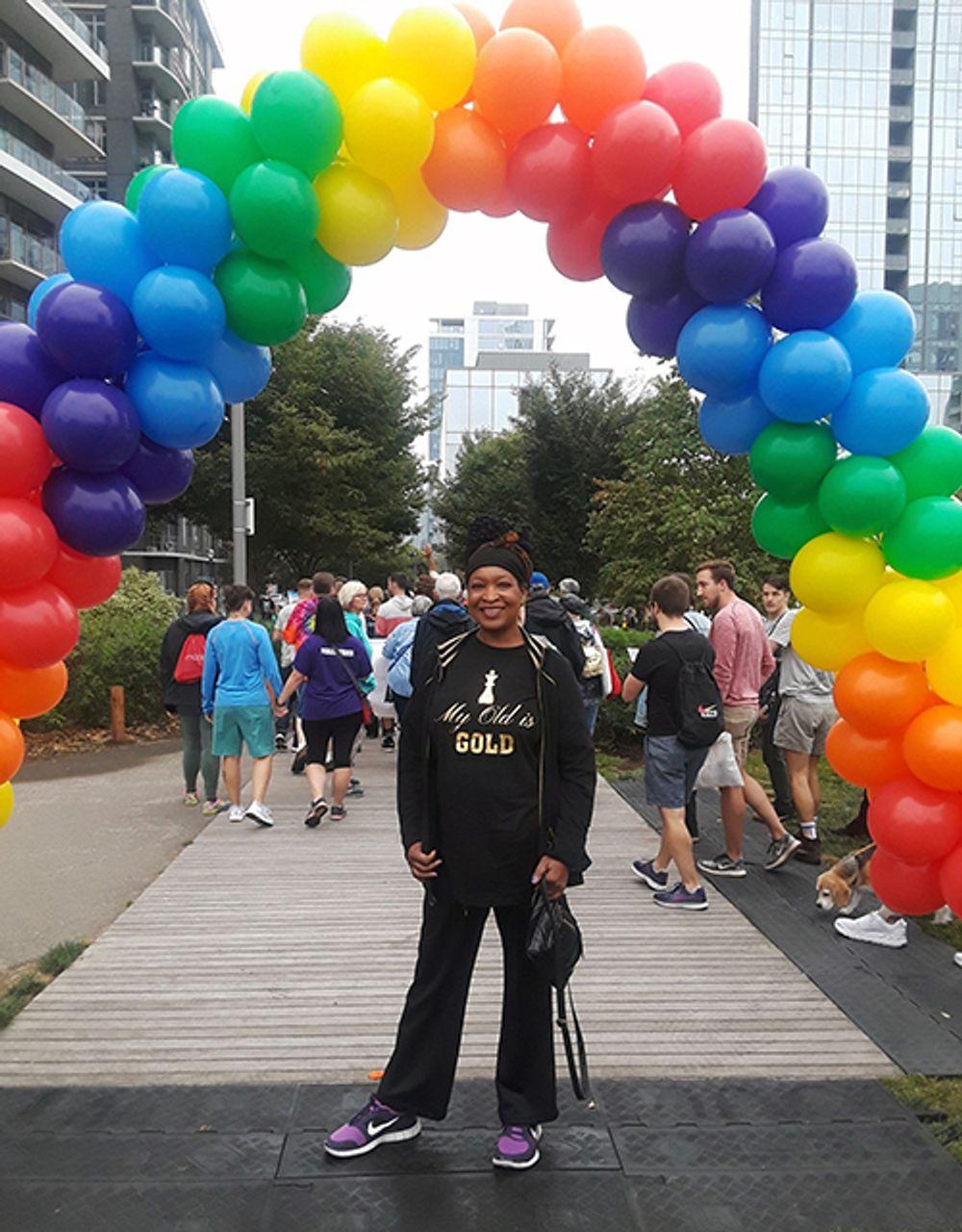 A Black woman under an arc of rainbow balloons