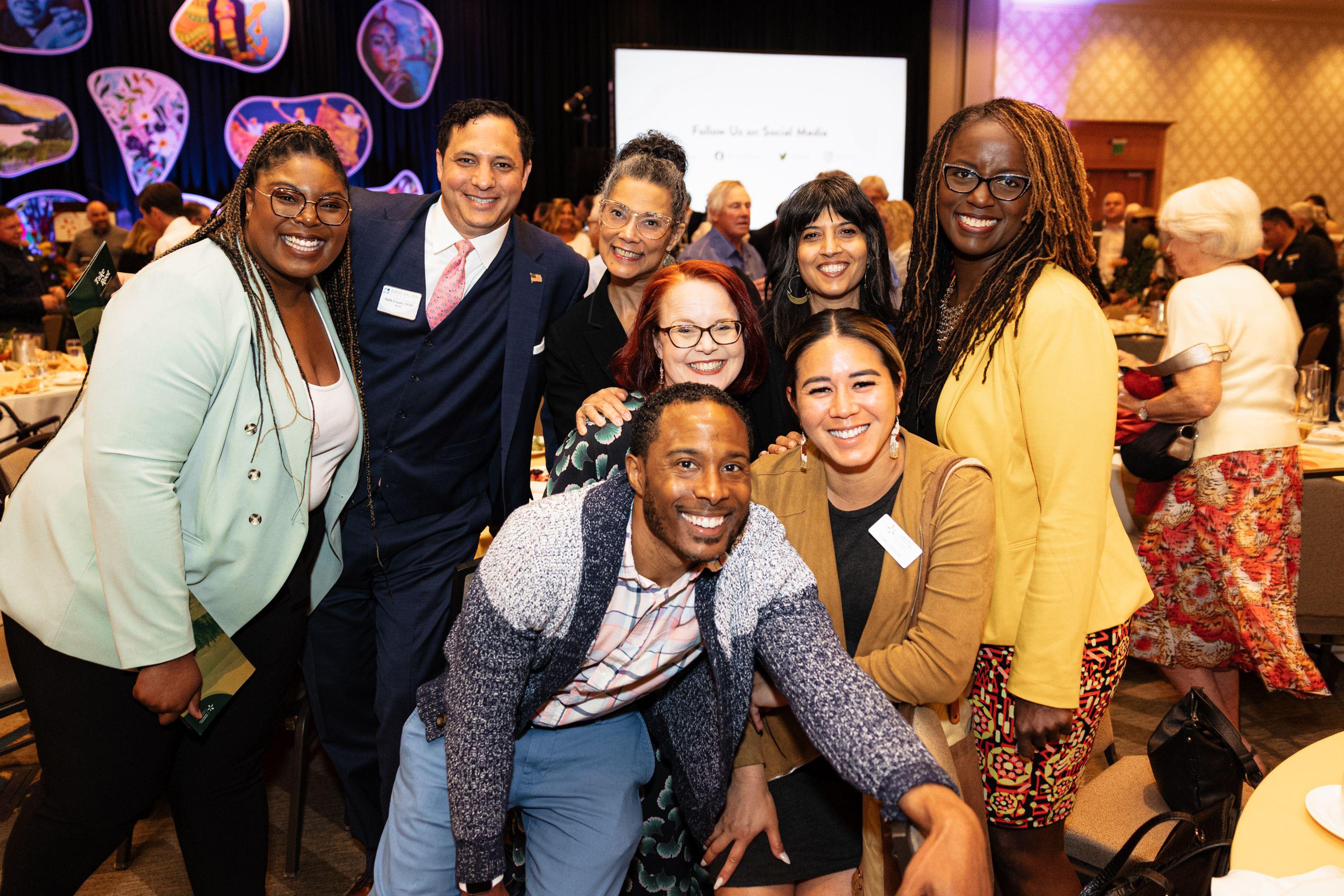 Large group of black, brown and white people smiling at the camera at our Annual Luncheon, Take Root, in 2023