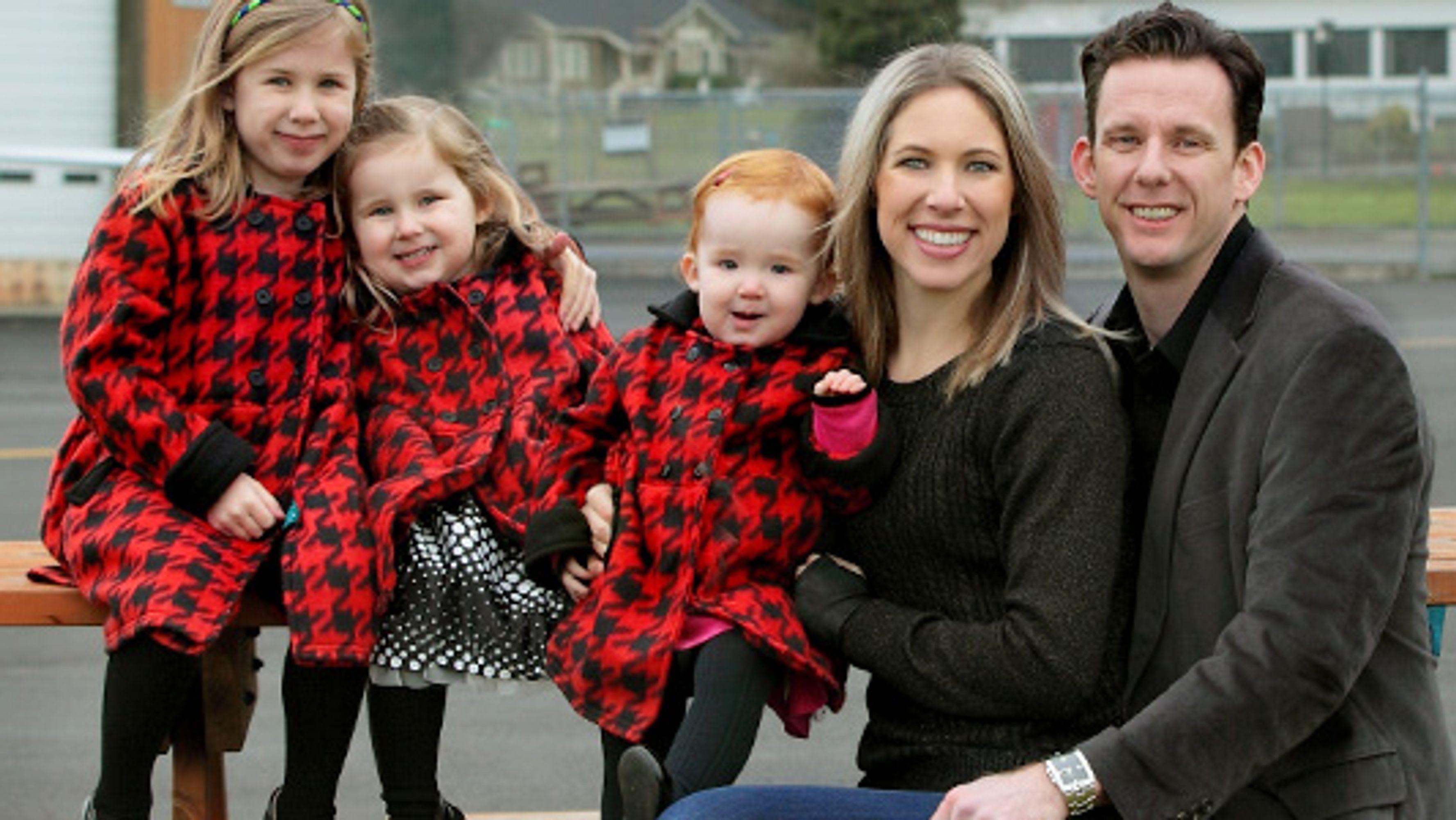 Three small children in matching coats with a smiling blonde woman and a smiling dark haired man