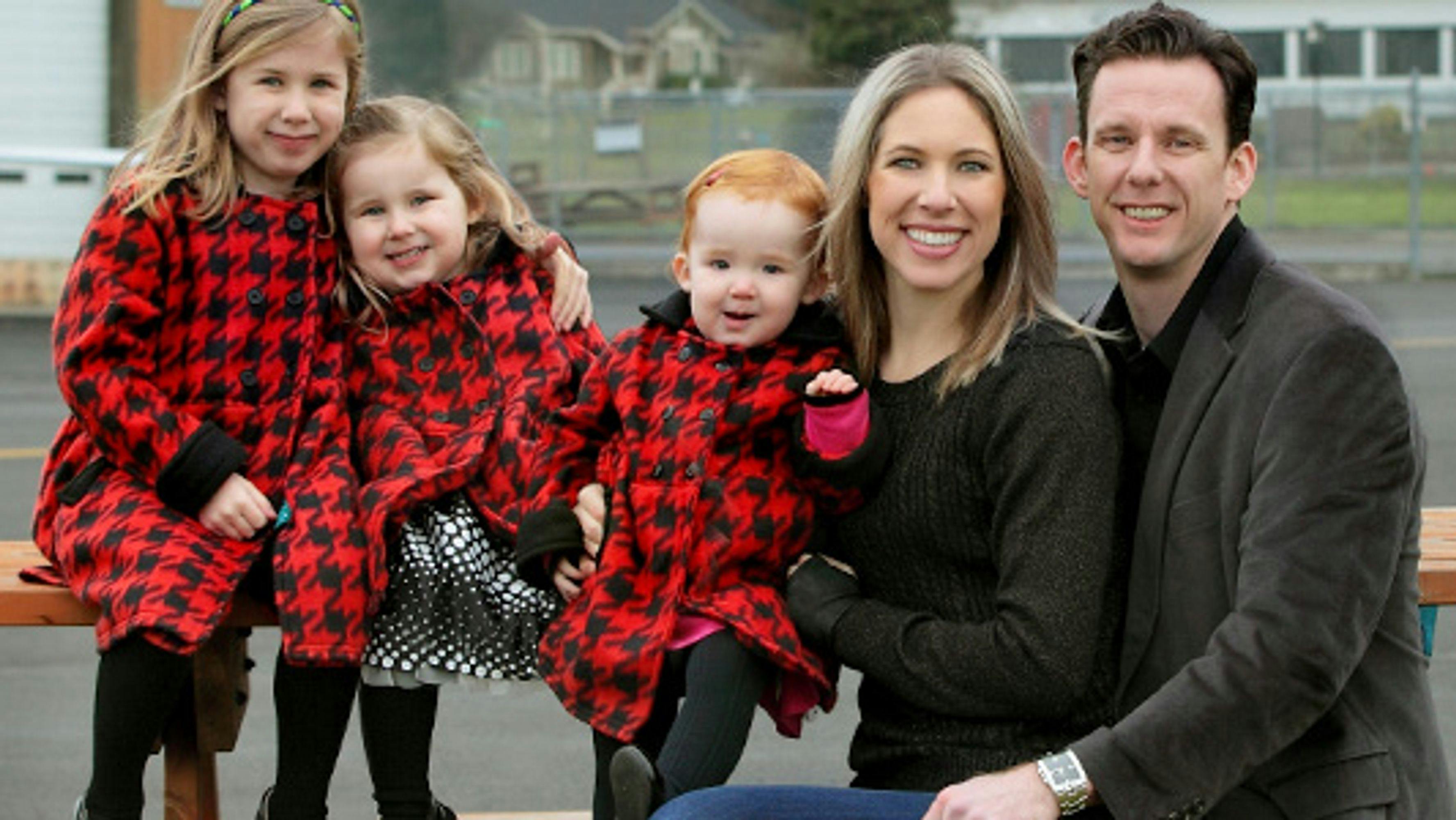 Three small children in matching coats with a smiling blonde woman and a smiling dark haired man