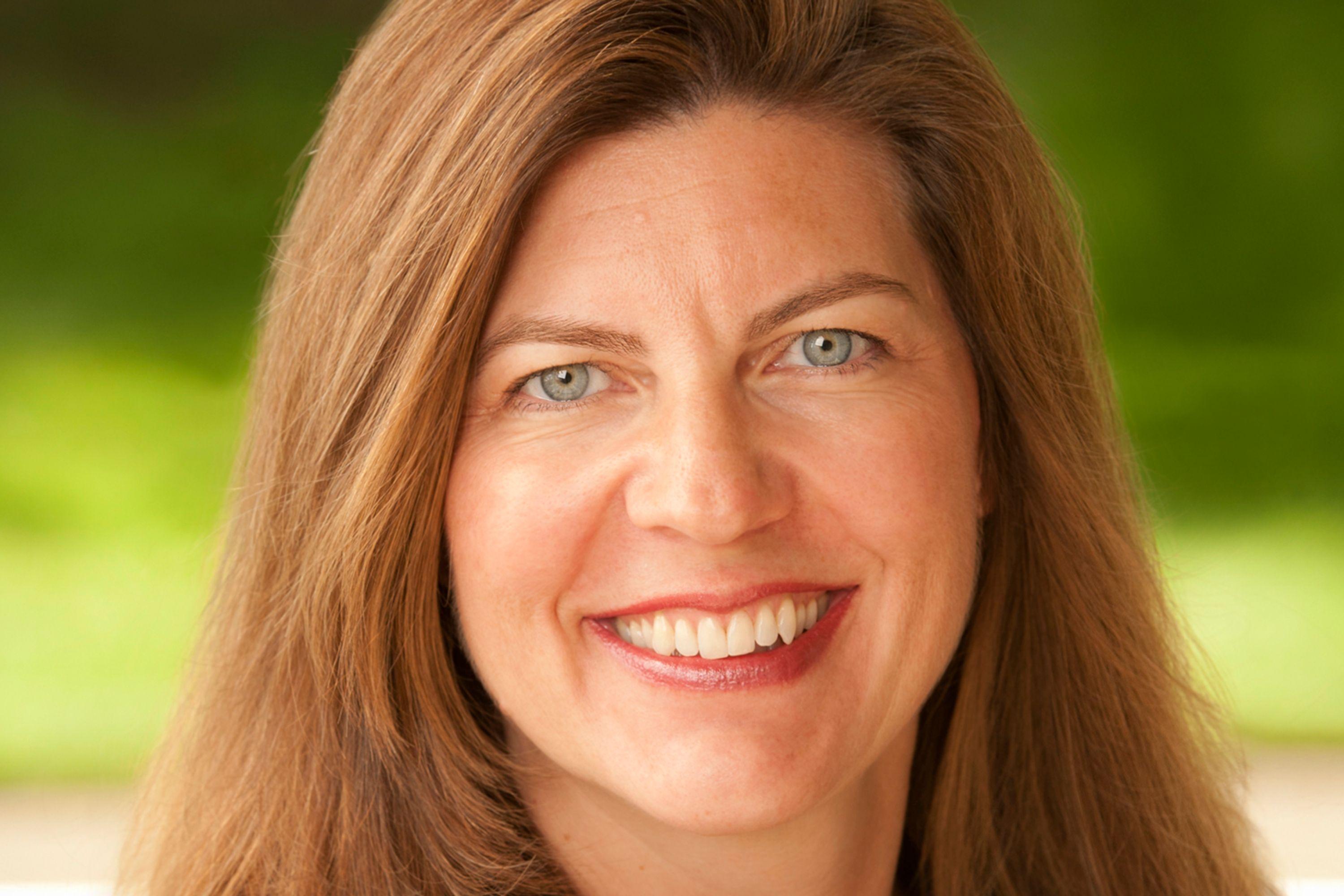 A headshot of Jennifer Rhoads smiling while wearing a gray blazer and black dress shirt.