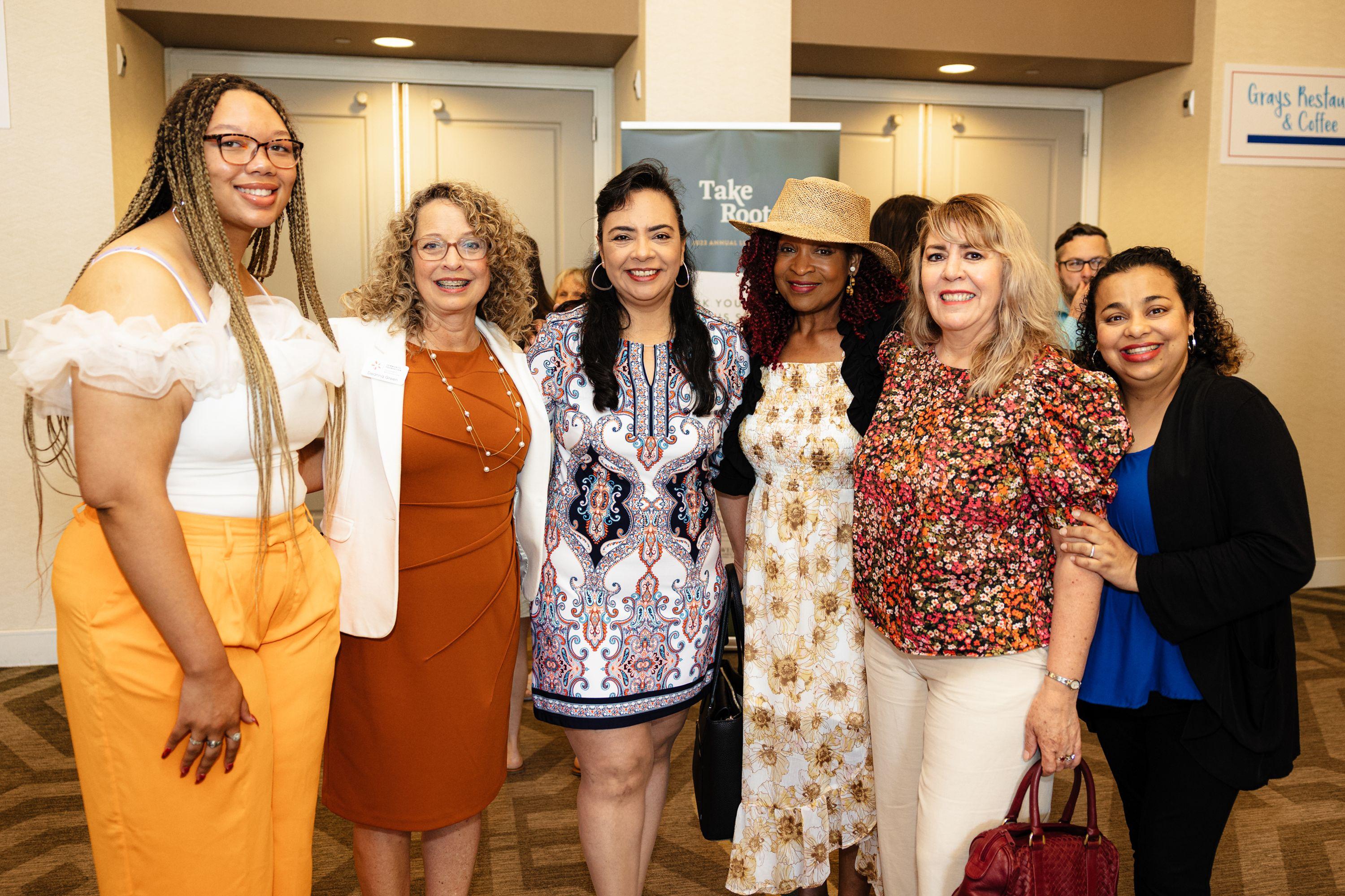 Six women, including Deanna Green and Karen Morrison, standing together and smiling in the lobby of our 2023 Annual Luncheon, Take Root