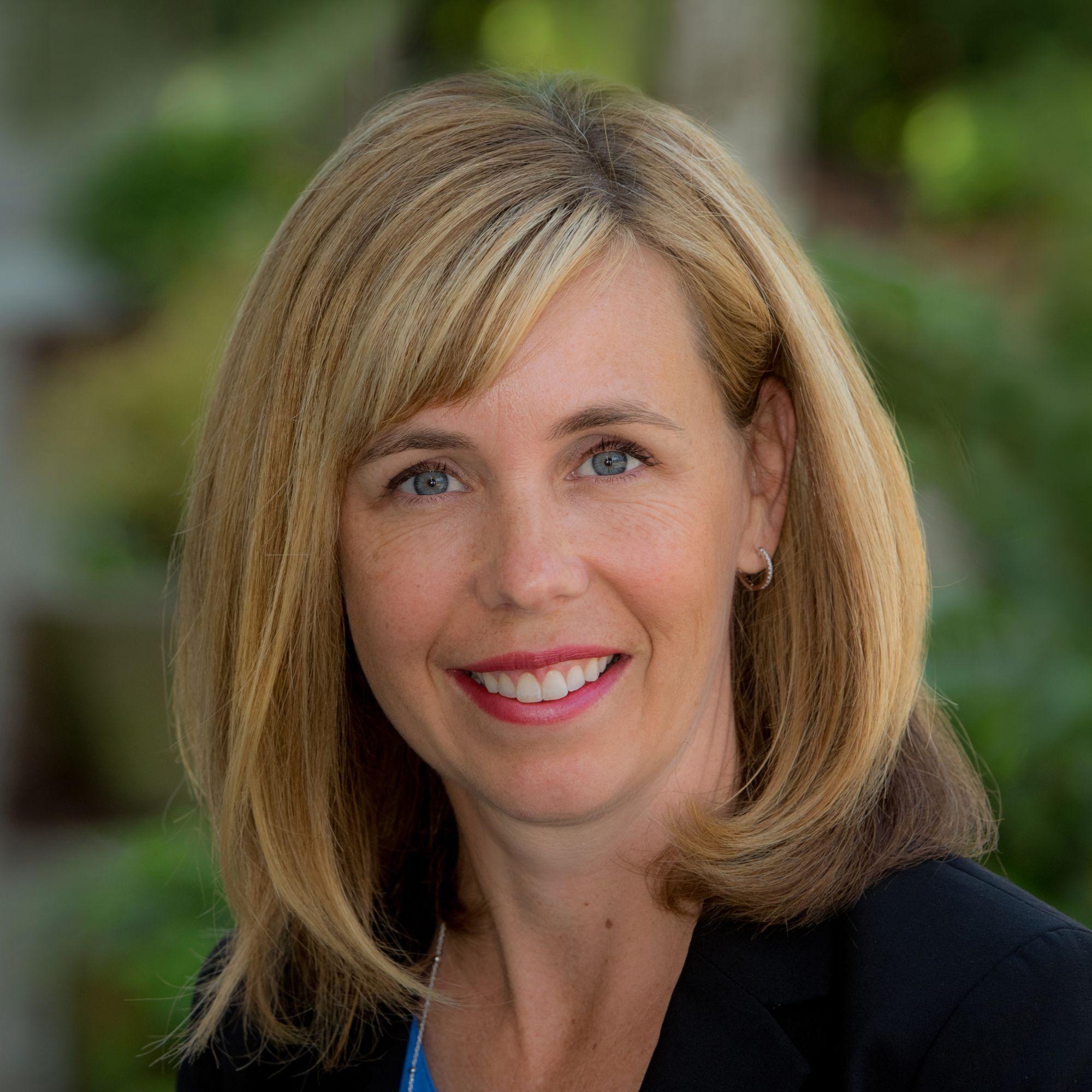 A blonde woman with a blue dress shirt and black blazer