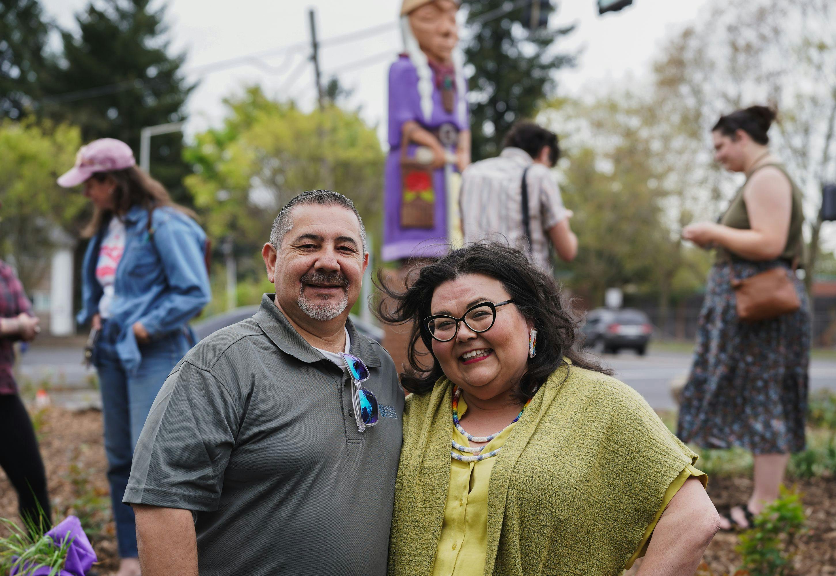 Shelia Davis smiling brightly at the camera in front of the Grandmother Camus art piece in the Fourth Plain neighborhood