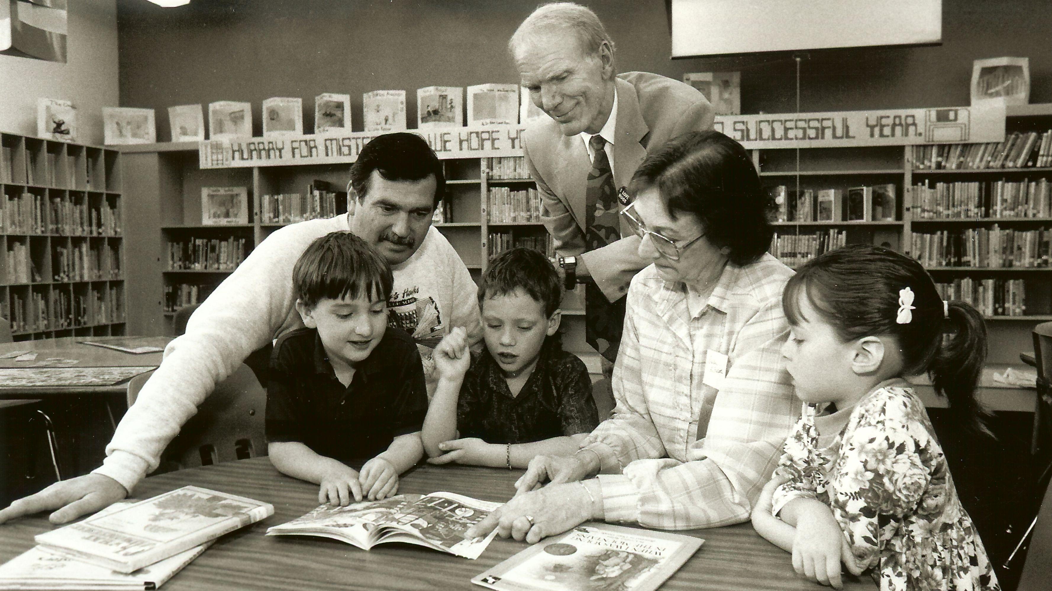 Paul Christensen standing over a group of young schoolchildren with a teacher in a school library