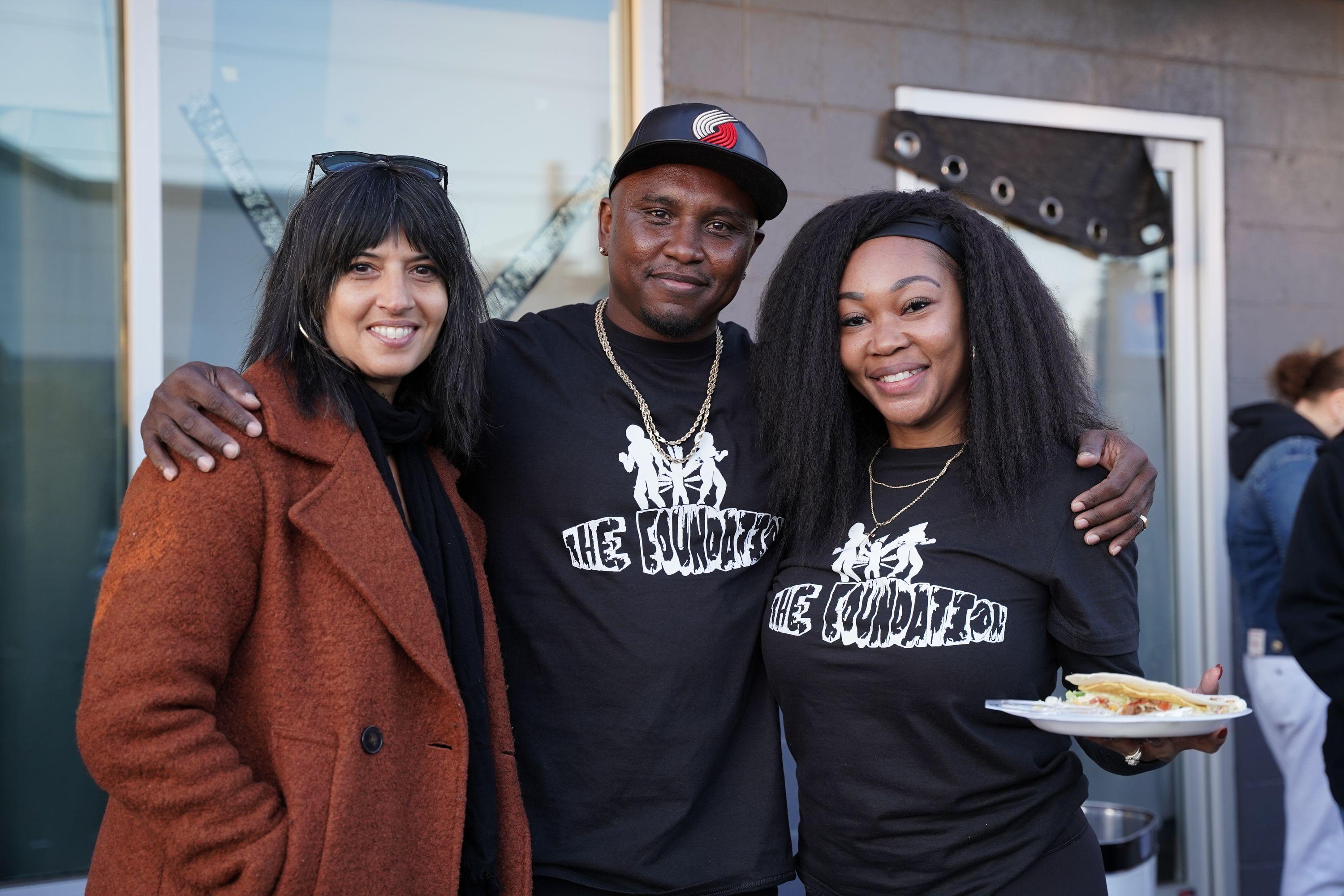 An Indian woman, a Black man, and a Black woman standing together smiling at the camera