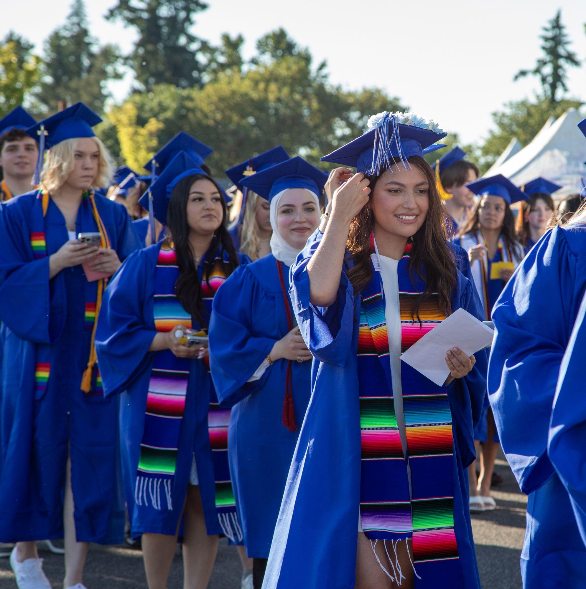 A Clark College graduate in her cap and gown adjusts her tassel while walking to her commencement ceremony. 