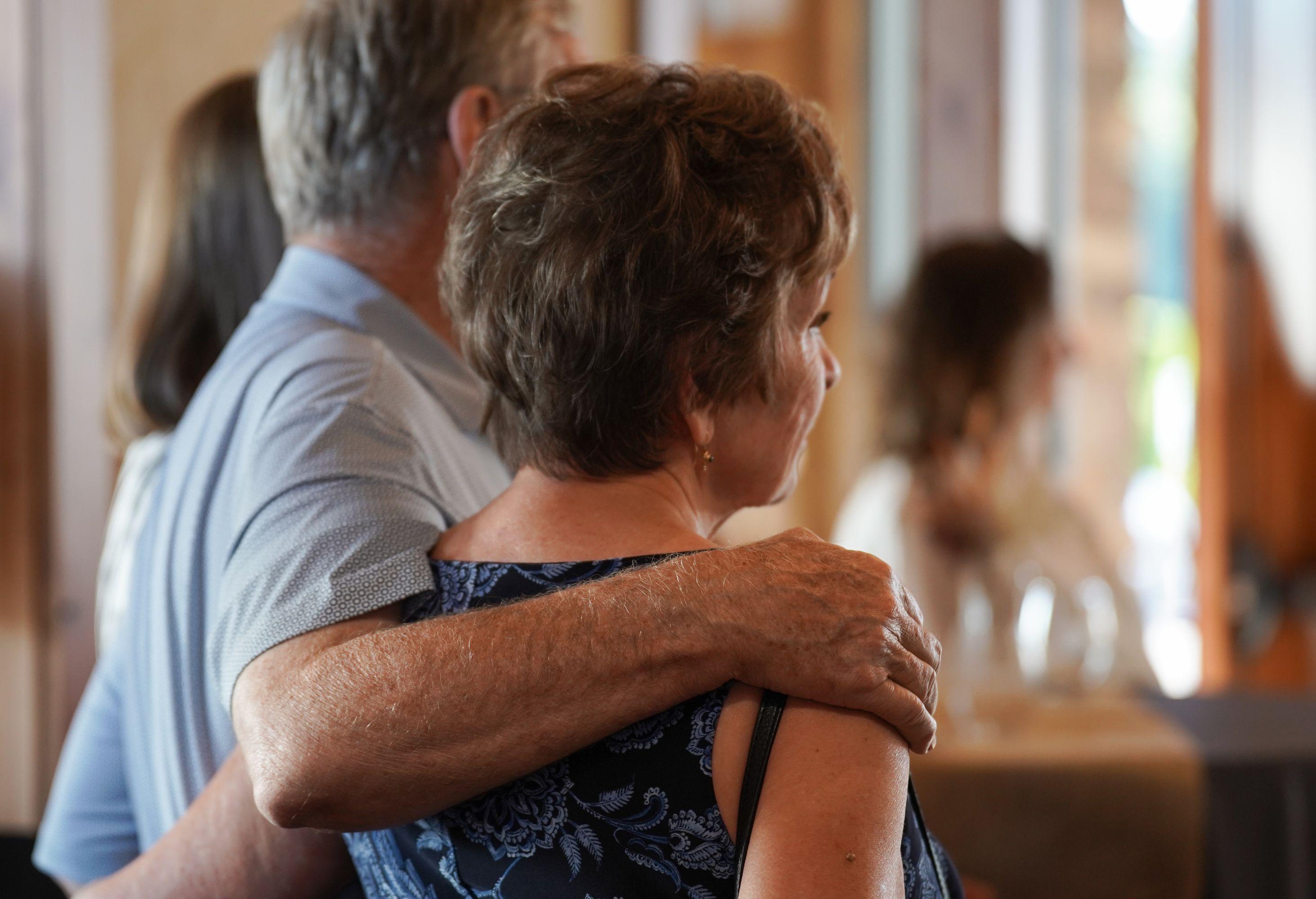 A couple standing next to each other, the man's arm around the woman's shoulder, with their backs to the camera