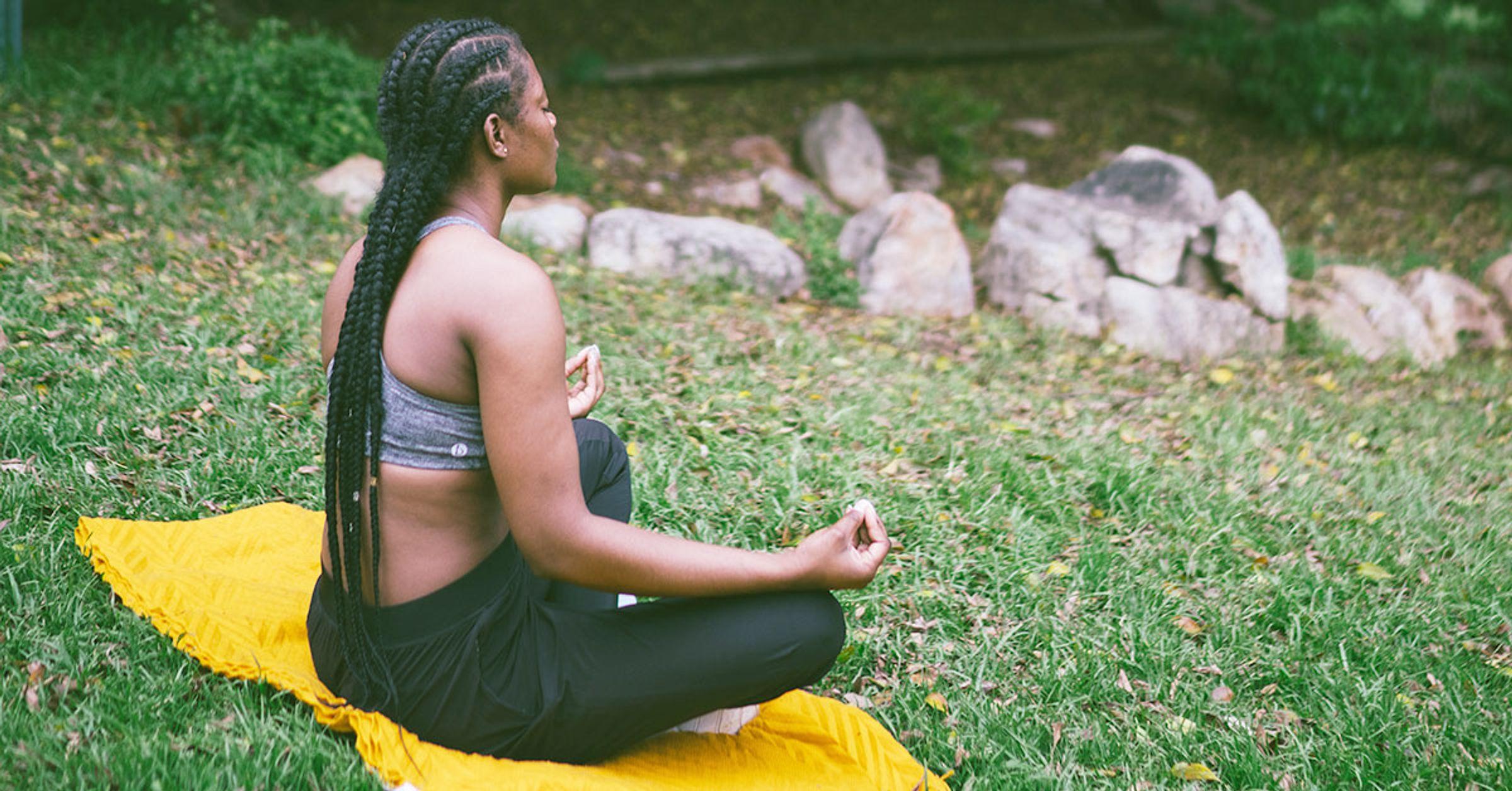 A black person meditating on a blanket outside