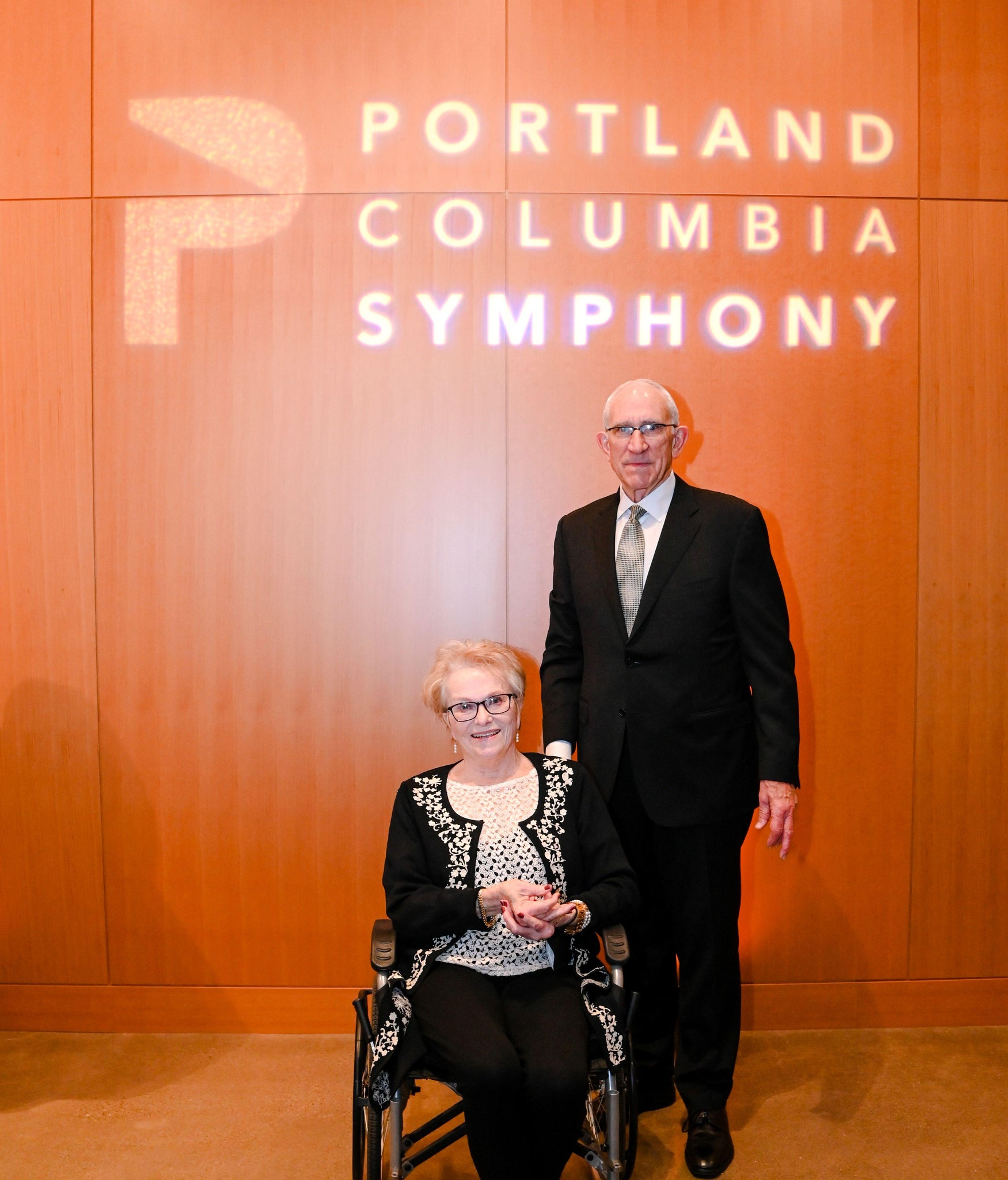 Greg and Betsy Hatton smiling in front of the Portland Columbia Symphony.